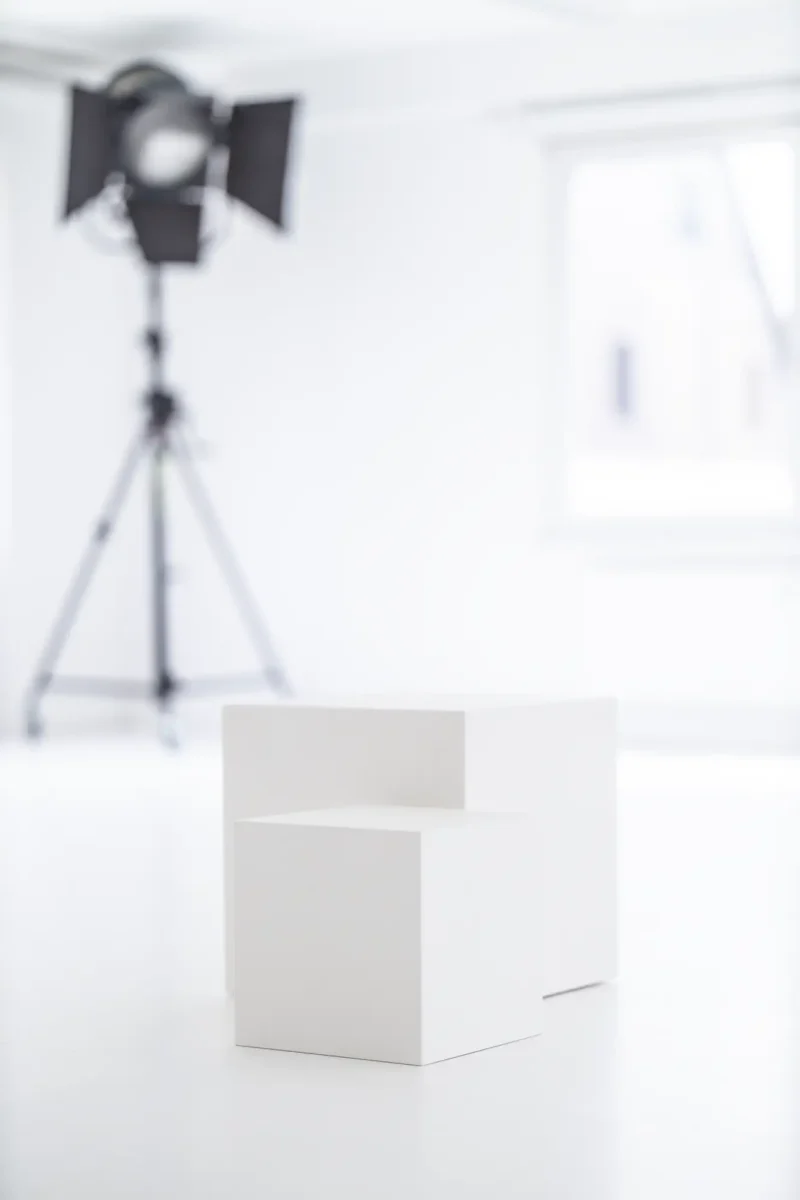 Tageslichtstudio mit zwei weißen Quadern als Sitz- oder Präsentationsobjekte vor weißen Wänden und großem Fenster